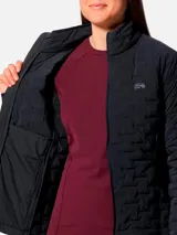 Campera técnica de plumón para mujer, color gris oscuro, con diseño de compartimentos elásticos integrados. Cuenta con cierre frontal completo, cuello alto, bolsillos laterales con cierre y puños con ribete elástico. Es una prenda compresible diseñada para actividades de montaña y senderismo.