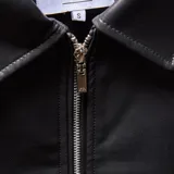 Campera de cuero sintético color negro, con cuello camisero, cierre frontal metálico, bolsillos laterales diagonales y puños con botón metálico.