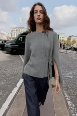 Chaqueta de punto gris con cuello redondo, manga larga acampanada y cierre frontal cruzado con botón y lazada lateral.