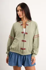 Campera oversize color crudo de algodón con spandex, corte de largo intermedio, mangas largas con detalles de costuras en zigzag bordadas y un gran diseño bordado a mano de una flor en la espalda.