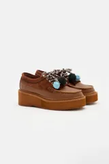 Zapato tipo mocasín de plataforma color bordó, confeccionado en una combinación de cuero liso y gamuza. Presenta cordones bicolores con detalle de borlas decorativas en el empeine.