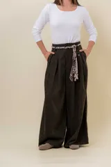 Pantalón wide leg de tiro alto en color negro, con diseño de pinzas delanteras que aportan volumen y caída fluida. Incluye bolsillos laterales y un lazo desmontable en la cintura que combina cordón con cinta de estampado animal print.
