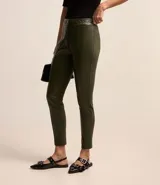 Pantalón legging color beige con frente de poliuretano que imita cuero y parte trasera de punto roma. Presenta detalle de cadena metálica en la cintura y cierre frontal.