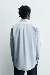 Camisa de corte regular fit confeccionada en tejido de algodón con estampado de microcuadros. Presenta cuello abotonado, manga larga con puños abotonados y cierre frontal con botones.