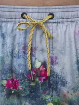 Short de baño con estampado botánico en tonos naranja y coral, con cintura elástica ajustable mediante cordón y malla interior para mayor soporte.