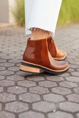 Botas tipo Chelsea de cuero, con diseño de paneles combinados en texturas lisas, gamuzadas y con relieve tipo reptil en el talón. Presentan una suela plana con taco bajo de madera y base de goma negra.