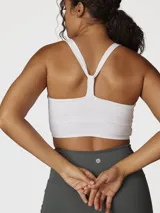 Top deportivo blanco de sujeción media con espalda cruzada, confeccionado con tecnología Aloe Vera para una textura suave y elástica.