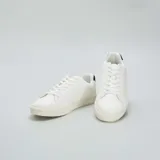 Zapatillas blancas de cuero sintético con cordones, suela plana y detalle de refuerzo negro en el talón.