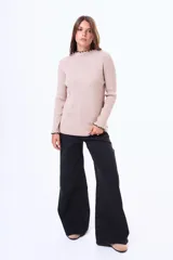 Buzo de tejido de punto acanalado en color beige, con cuello alto y terminaciones con borde ondulado en contraste negro en cuello y puños.