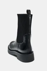 Botín de estilo urbano con suela track, confeccionado en cuero sintético negro con caña de tejido elástico acanalado. Presenta punta redonda, tirador trasero y diseño tipo pull-on.