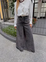 Pantalón de jean estilo wide leg en color gris oscuro con efecto lavado. Presenta un corte de tiro alto, costuras verticales marcadas en el frente y una silueta amplia y fluida.