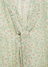 Blusa de gasa estampada con flores, de corte recto y diseño semitransparente. Tiene cuello pico con lazo, cierre frontal con botones y mangas largas con puños elásticos. Incluye forro interior.