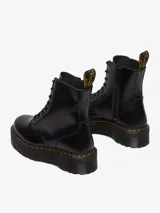 Borcego negro de cuero liso pulido, con plataforma gruesa y suela ranurada. Presenta costuras amarillas distintivas, cordones negros y una cremallera interior para facilitar su calce. Incluye el clásico lazo negro y amarillo en el talón.