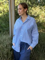 Camisa celeste a rayas verticales blancas, de corte holgado, manga larga y cuello camisero.