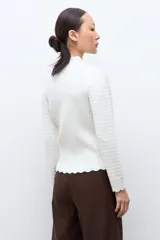 Sweater de punto color crudo con cuello medio alto, manga larga y diseño de textura acanalada con terminación festoneada en el ruedo.