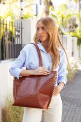 Bolso tipo tote de cuero color marrón con textura tipo cocodrilo, doble asa de hombro y cierre superior con cremallera.