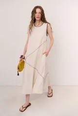 Vestido midi sin mangas de corte holgado y silueta acampanada, color beige con costuras decorativas diagonales en contraste marrón. Cuenta con cuello redondo y bolsillos laterales.