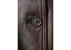 Chaqueta bomber de cuero ovino color marrón oscuro, con cierre frontal de botones, bolsillos con solapa en el pecho y cuello alto con broches.