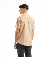 Camisa de manga corta color celeste claro, confeccionada en algodón, con cuello clásico y un bolsillo de parche en el lado izquierdo del pecho.