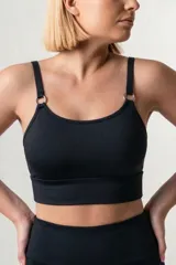 Top deportivo de escote redondo, con breteles finos que se conectan al cuerpo mediante aros metálicos. Presenta una faja ancha de doble tela en la base para mayor soporte.