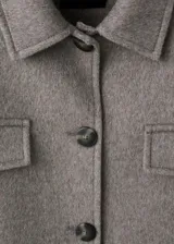Chaqueta estilo overshirt de paño color gris, con cuello solapa, cierre frontal de botones oscuros, bolsillos con solapa en el pecho y bolsillos aplicados en la parte inferior.