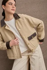 Campera corta de paño color marrón con detalles en cuero sintético al tono en cuello, puños y solapas de bolsillos. Presenta cierre frontal con botones metálicos dorados y dos bolsillos frontales tipo cargo.