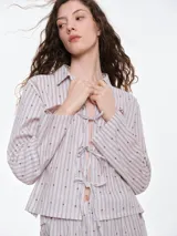 Camisa de dormir de popelina de algodón, con estampado de rayas verticales y pequeños motivos geométricos. Presenta cuello camisero, mangas largas y cierre frontal mediante lazos ajustables.