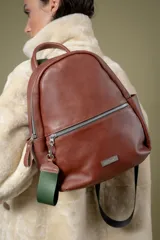 Mochila de cuero vacuno color marrón, con diseño de compartimento principal y bolsillo frontal con cierre metálico. Incluye correas de cinta regulables y detalle de tirador de cierre en color verde.