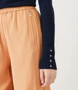 Suéter de punto color rosado, con cuello barco, mangas largas y puños con botones decorativos. El dobladillo también es acanalado.