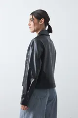 Chaqueta de cuero sintético negro con acabado brillante, cuello camisero, cierre frontal con botones a presión y bolsillos frontales con solapa.