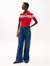 Chomba roja de piqué de algodón elástico con corte slim, cuello clásico, tapeta de seis botones y rayas horizontales blancas en el pecho y mangas. Logo de Tommy Hilfiger bordado en la manga.