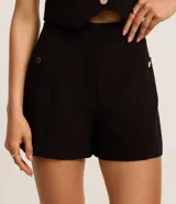 Short sastre de cintura alta color marrón, con bolsillos laterales y detalles de tachuelas metalizadas.