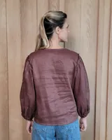 Camisa de manga larga con diseño de rayas verticales y bordados sutiles. Presenta cuello redondo, cierre frontal con botones y mangas abullonadas con volados en los hombros.