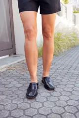 Zapatos tipo mules de cuero negro, con punta fina y detalle de charol en el borde superior.