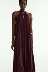 Vestido midi plisado color bordó, con cuello halter, broche de flor en el delantero y anudado en la espalda. Cuenta con forro interior.