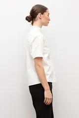 Camisa blanca de manga corta con cuello mao y detalles de volados a lo largo de la botonera frontal y en los puños.