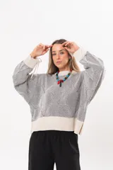 Buzo tejido de punto bicolor en tonos crudo y gris, con silueta relajada, mangas amplias con jaretas regulables en los puños y cuello redondo.