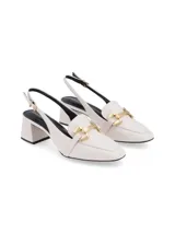 Zapato destalonado color crema de cuero napa, con taco cuadrado forrado, punta cuadrada y ornamento metálico dorado en el empeine. Cuenta con tira ajustable con hebilla en el talón.