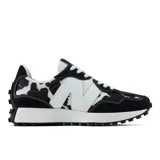 Championes New Balance 327 con diseño estampado tipo animal print de vaca en blanco y negro, superposiciones de gamuza negra, gran letra "N" blanca en el lateral y suela con relieve de inspiración trail.