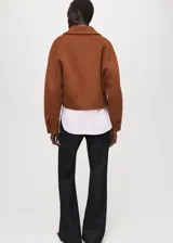 Chaqueta marrón de corte corto y diseño estructurado, con cuello solapa, cierre frontal de cremallera y mangas largas con puños anchos.