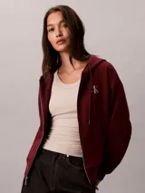 Campera canguro Calvin Klein de felpa color bordó, con capucha ajustable por cordones, cierre frontal completo de cremallera, mangas largas y bolsillos laterales. Presenta el logo monograma de la marca bordado en el pecho.