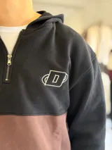 Hoodie de felpa con capucha y medio cierre frontal, diseño en bloques de color celeste y blanco, con bordados decorativos en el pecho.