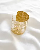 Pulsera tipo brazalete rígido dorado con textura ondulada.