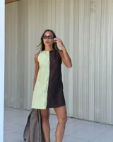 Vestido corto de diseño bicolor con paneles verticales en verde claro y marrón oscuro. Presenta un escote recto, corte sin mangas y una textura arrugada en la tela. Incluye bolsillos laterales ocultos y cierre en la espalda.
