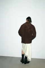 Chaqueta tipo blazer oversize de piel de ante color marrón oscuro, con cuello solapa de muescas, manga larga y bolsillos delanteros con solapa. Cierre frontal con botones.