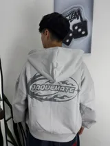 Campera tipo hoodie gris con capucha, de corte boxy y diseño holgado. Presenta un estampado gráfico en la espalda con la palabra Jaquemate rodeada de elementos de fuego y una estrella.