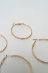 Set de siete pares de aros dorados de diversos estilos, incluyendo tres pares de aros tipo argolla de diferentes tamaños y texturas, y cuatro pares de aros pequeños con diseños variados como perlas, brillantes y formas geométricas.