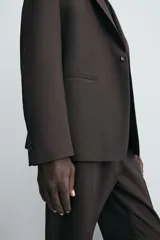 Blazer de corte regular fit confeccionado en tejido con lana. Presenta cuello con solapas de muesca, cierre frontal de un botón, bolsillos de vivo en el pecho y en la cadera, y aberturas en la espalda.