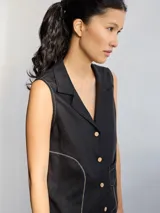 Camisa sin mangas de lino, color blanco, con cuello solapa, cierre frontal con botones y bolsillo pequeño en el pecho. Presenta costuras decorativas a la vista que definen la silueta.