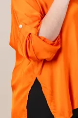 Camisa italiana de satén color naranja, de calce holgado, con manga caída y presilla para sujetar la manga. Presenta tajos a los costados y botones de nácar.